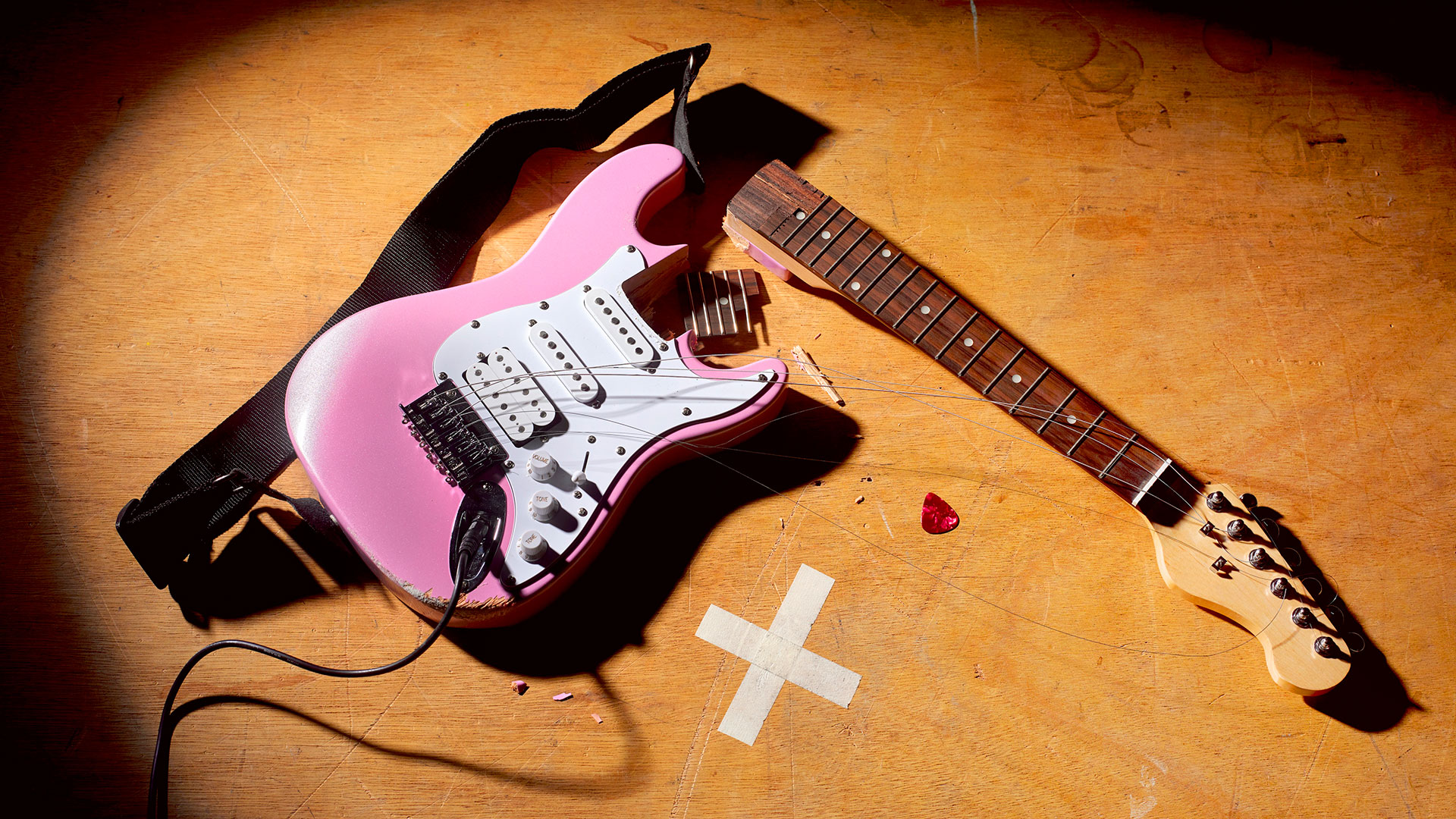 A smashed pink Stratocaster style guitar lies on a wooden floor