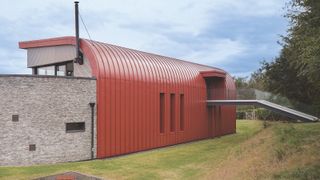 curved corten red roof around self build house