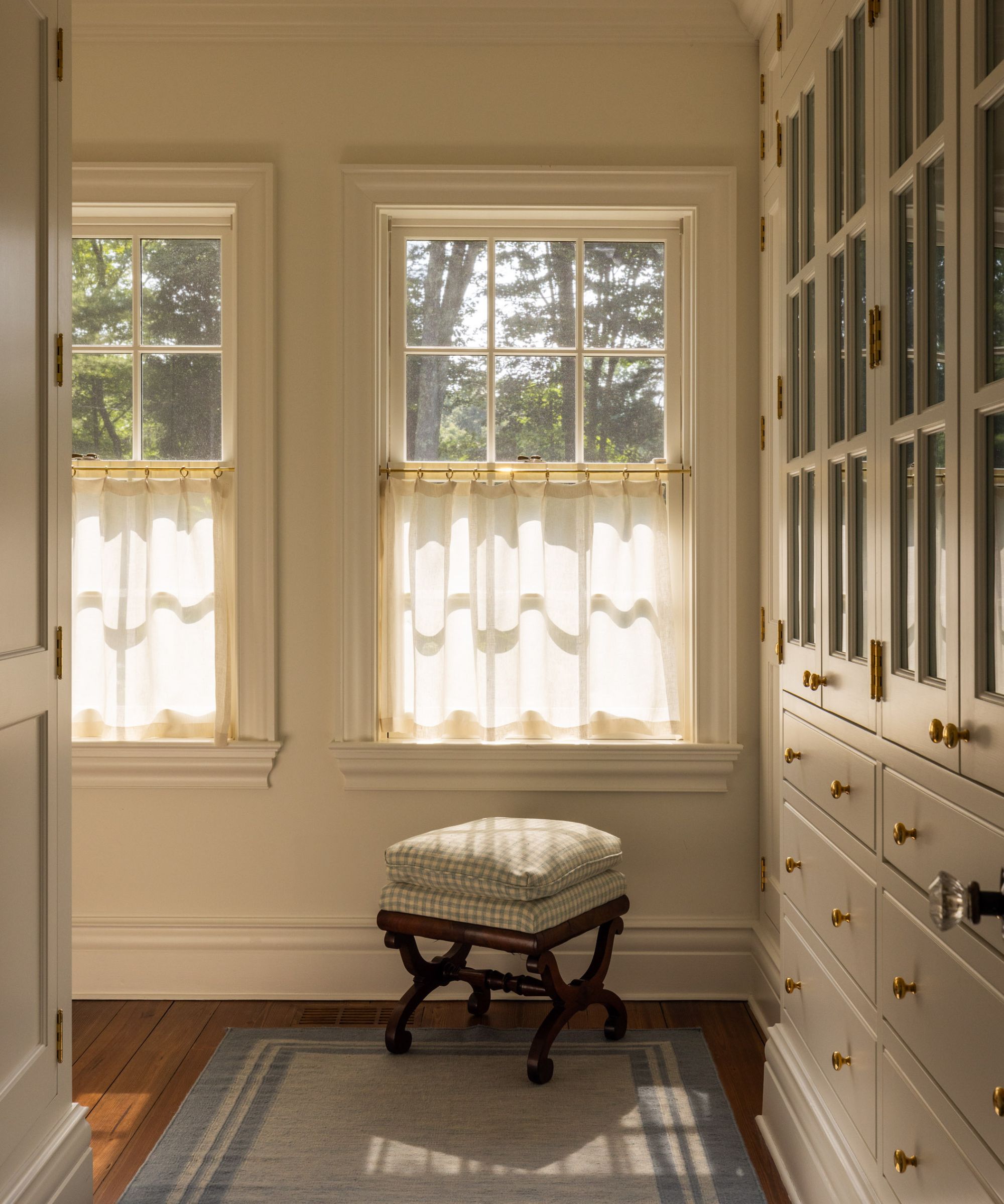 Closet with built in cabinets and windows and blue rug and gingham stool