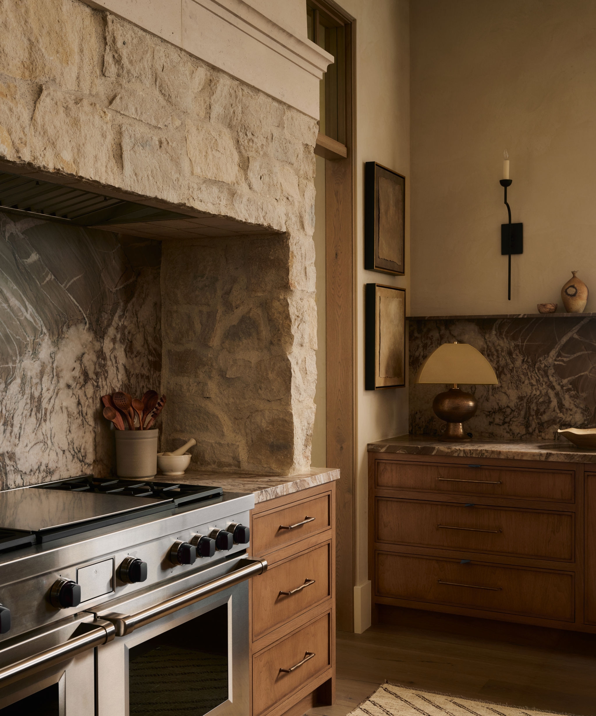 A neutral kitchen with wood cabinets, stone countertops, a stainless steel range, and exposed stone