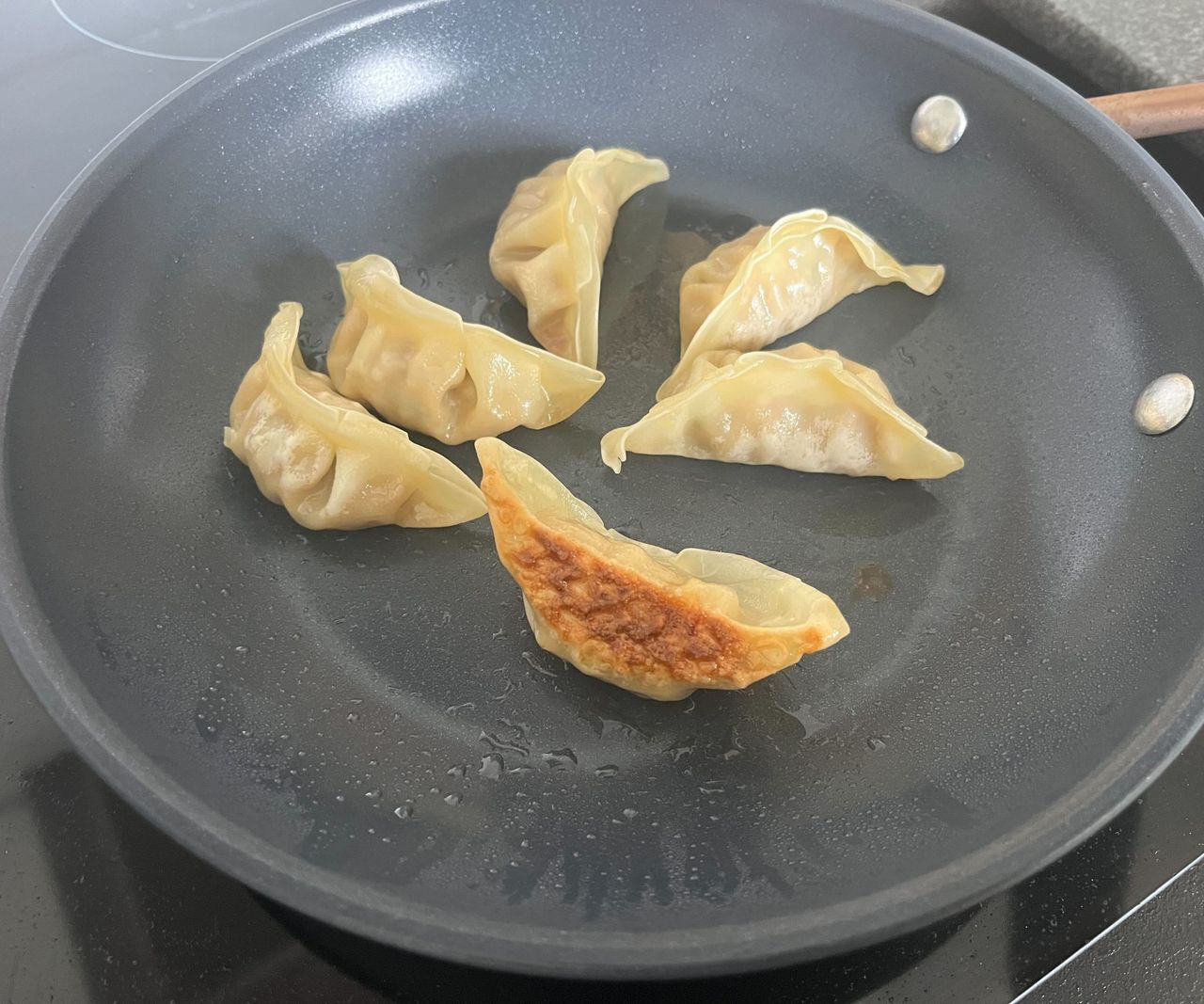 Gyoza frying in a small blue ceramic frying pan, one on its side to show the golden crisp base