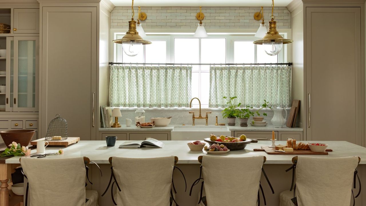 soft beige kitchen designed by Oho Interiors with a large island styled with linen breakfast bar chairs and two antique style brass pendant lights