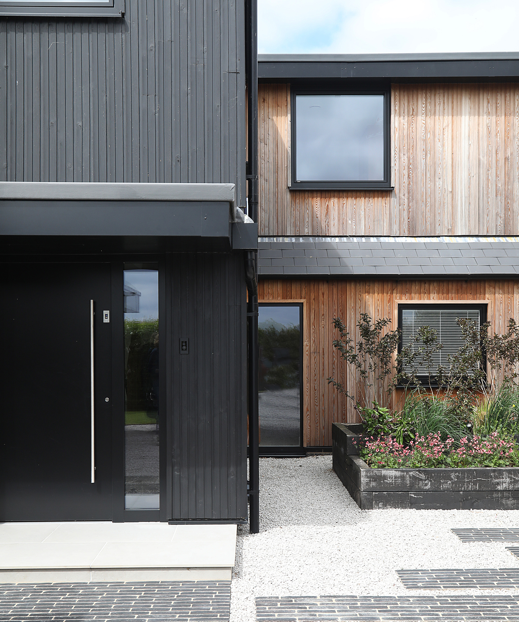 A front garden landscaped with gravel and planting beds  in front of a contemporary renovation of a 1980s home