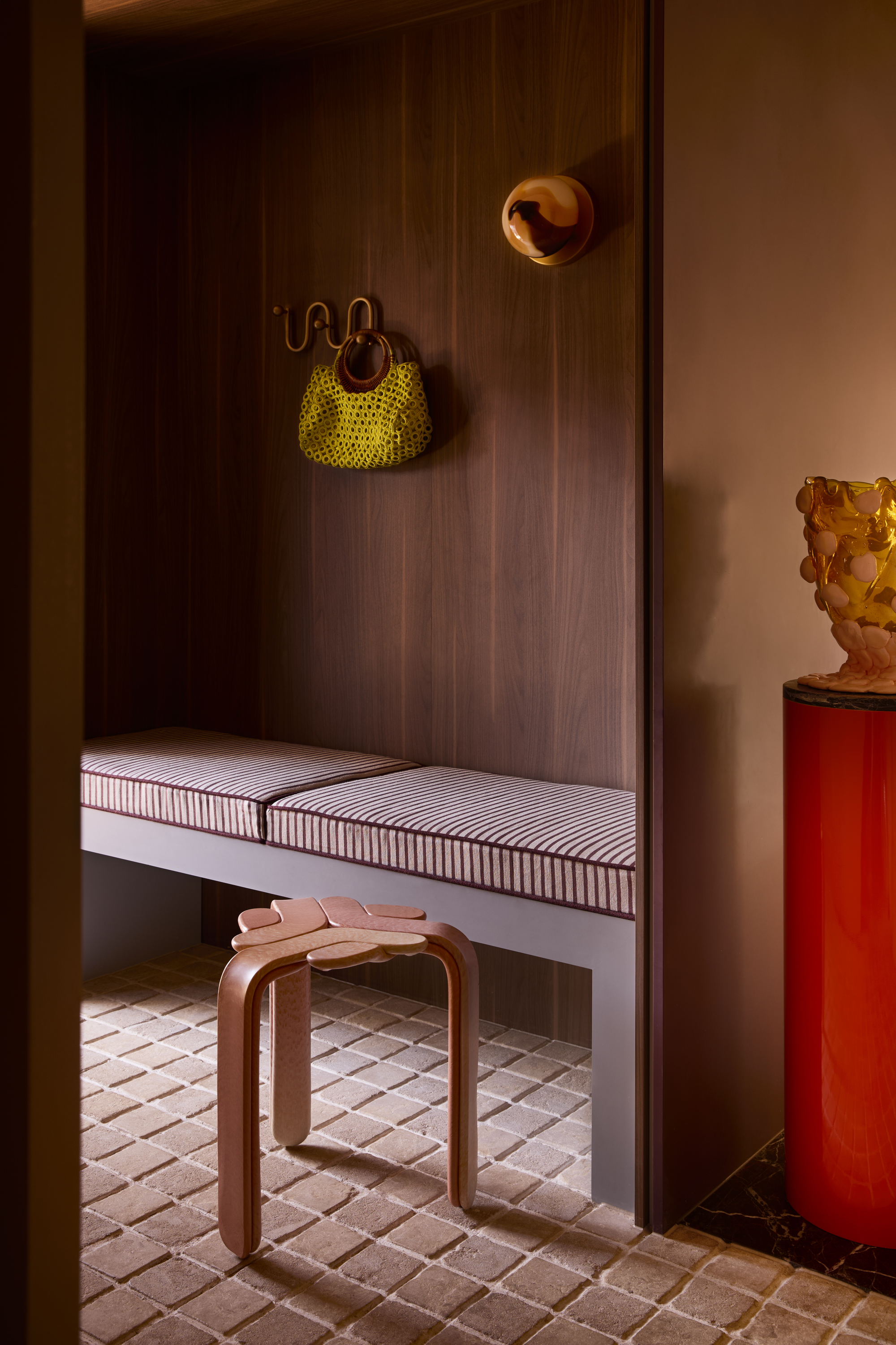 entryway with a striped upholstered bench seat, timber wall and cobblestone floor
