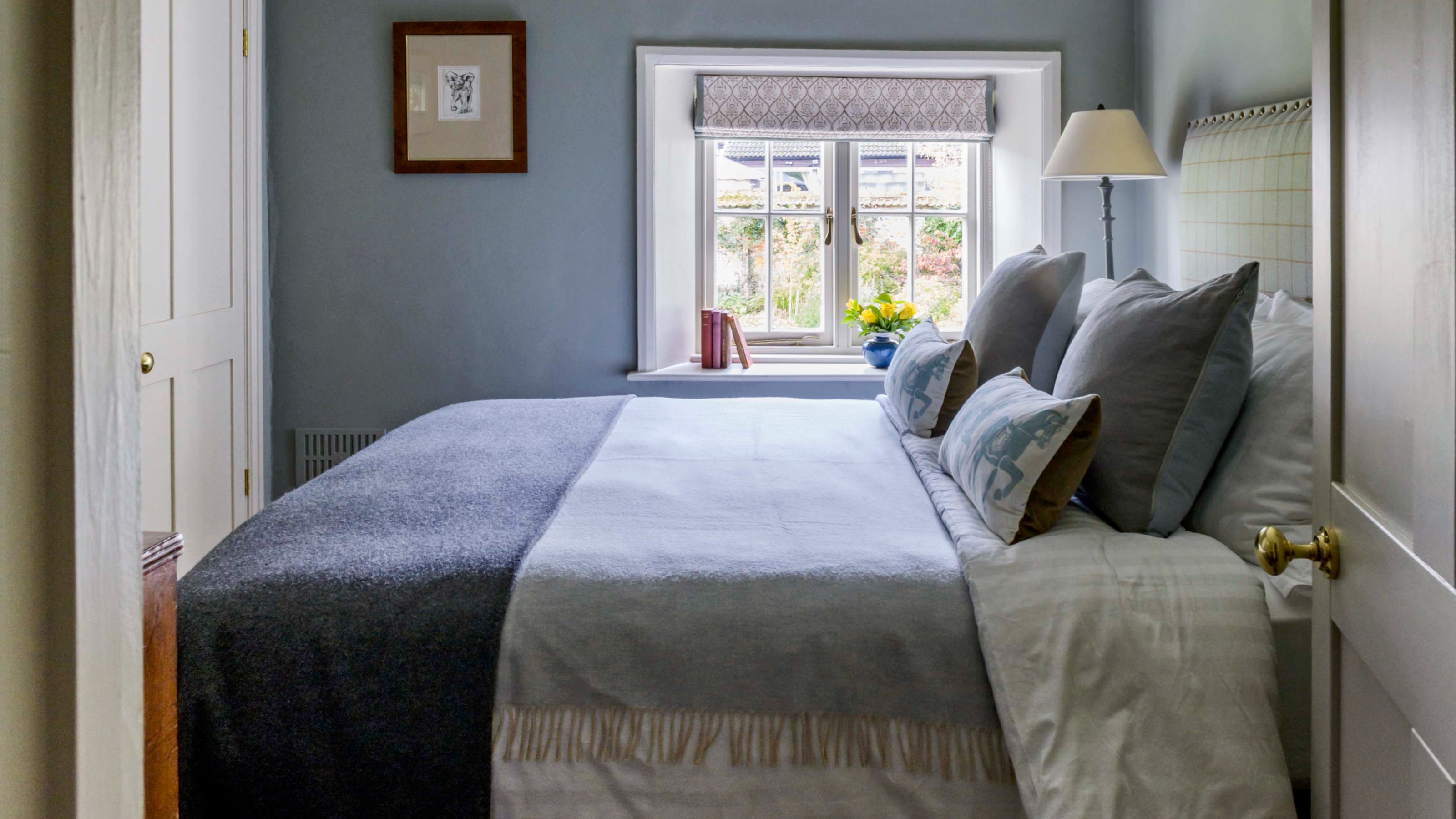A box bedroom painted in blue with grey undertone and a bed in the middle with tonal bed linen