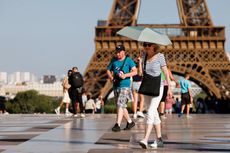 A senior woman holding an umbrella to block the sun while walking in front of the Eiffel Tower