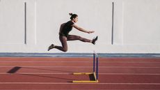 A woman jumps over a hurdle on a running track.