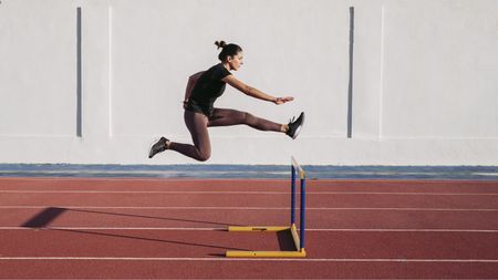 A woman jumps over a hurdle on a running track.