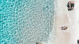 People lying in the sand at the water's edge of La Marinedda beach, Sardinia