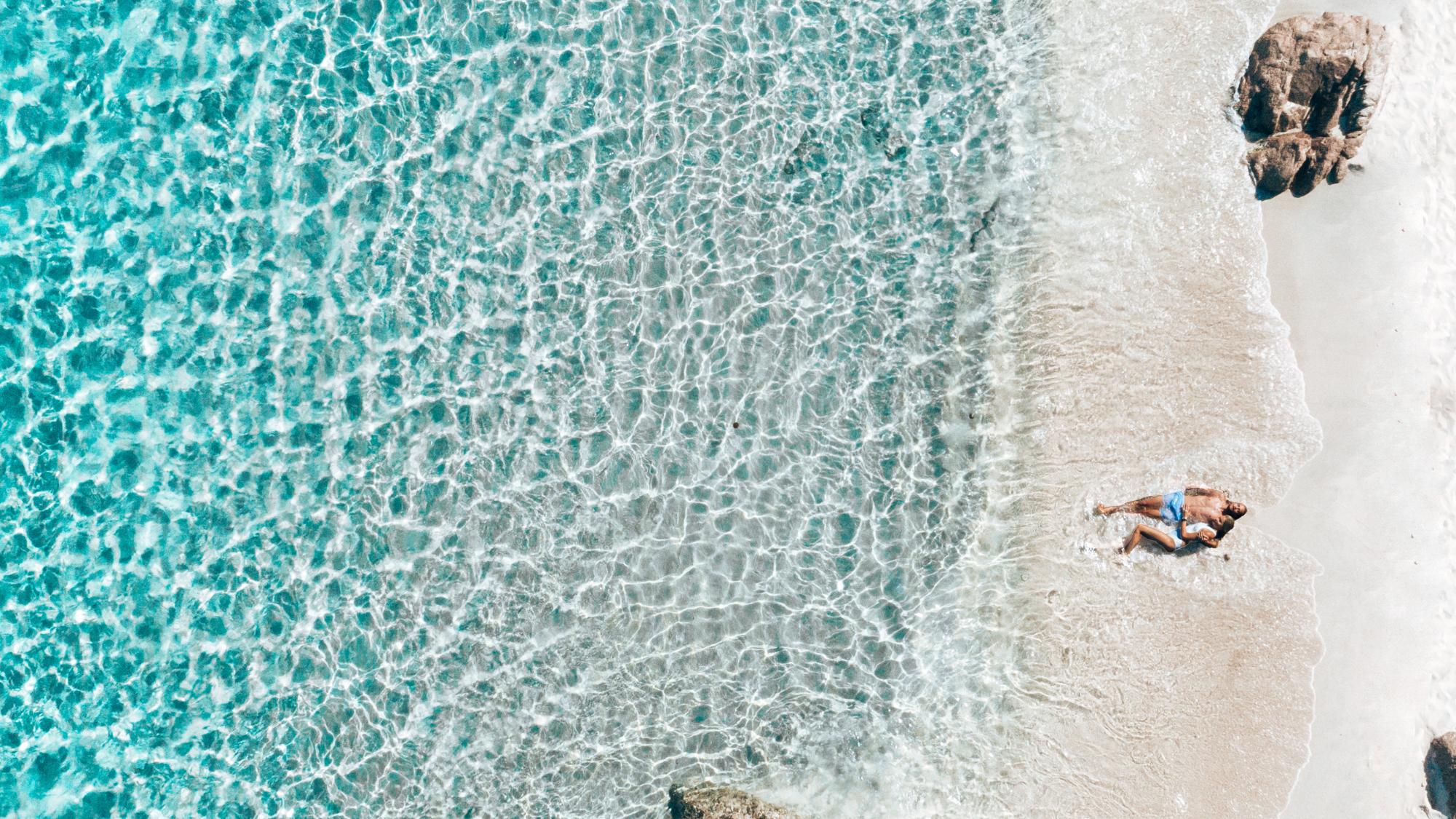 People lying in the sand at the water's edge of La Marinedda beach, Sardinia