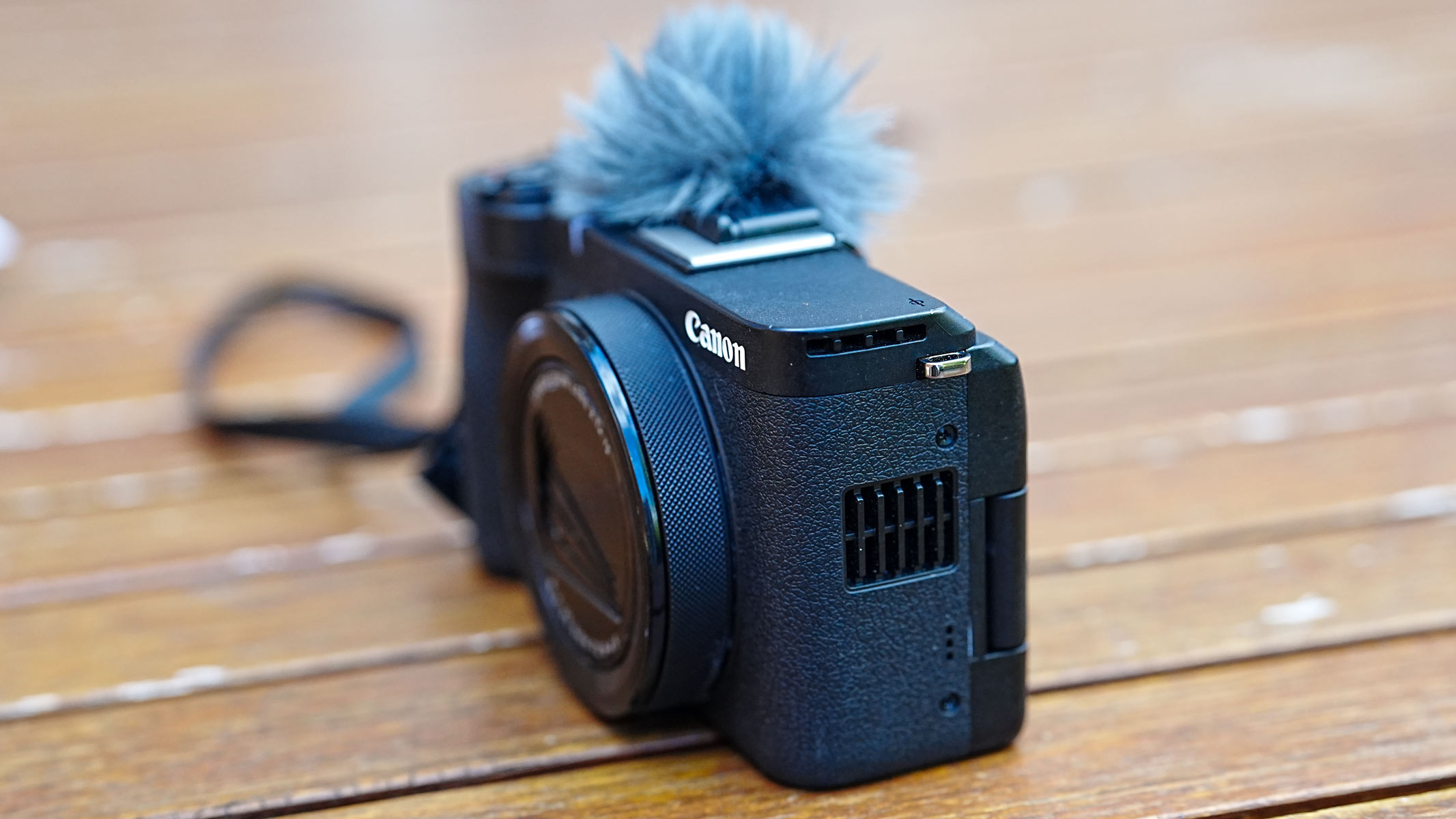 The Canon Powershot V1 on a wooden table with shutter closed and deadcat microphone cover.