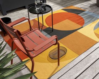 A multicoloured outdoor rug with a red metal garden chair