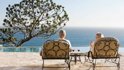 A retired couple lounge at a pool overlooking the ocean.