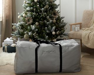The White Company branded Christmas tree storage bag positioned in front of artificial Christmas tree decorated with lights and decorations