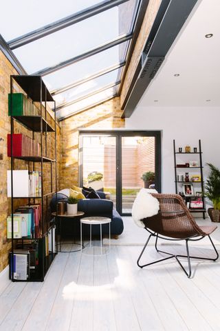 inside a side return extension with a fully glass/window ceiling, brick walls on the side extension, furniture and white wooden floors