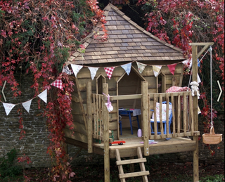 Wooden raised children's outside playhouse with bunting in a garden
