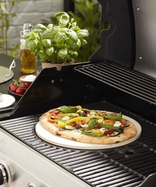 Pizza cooking on a pizza stone on a grill