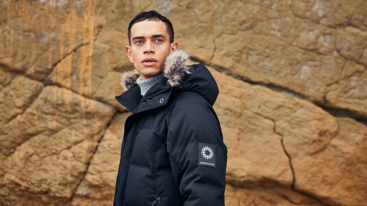 Man surrounded by rocks, he&#039;s wearing one of the best winter coats, the Shackleton Lockroy parka