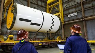 two people in hard hats looking up at a rocket on a crane
