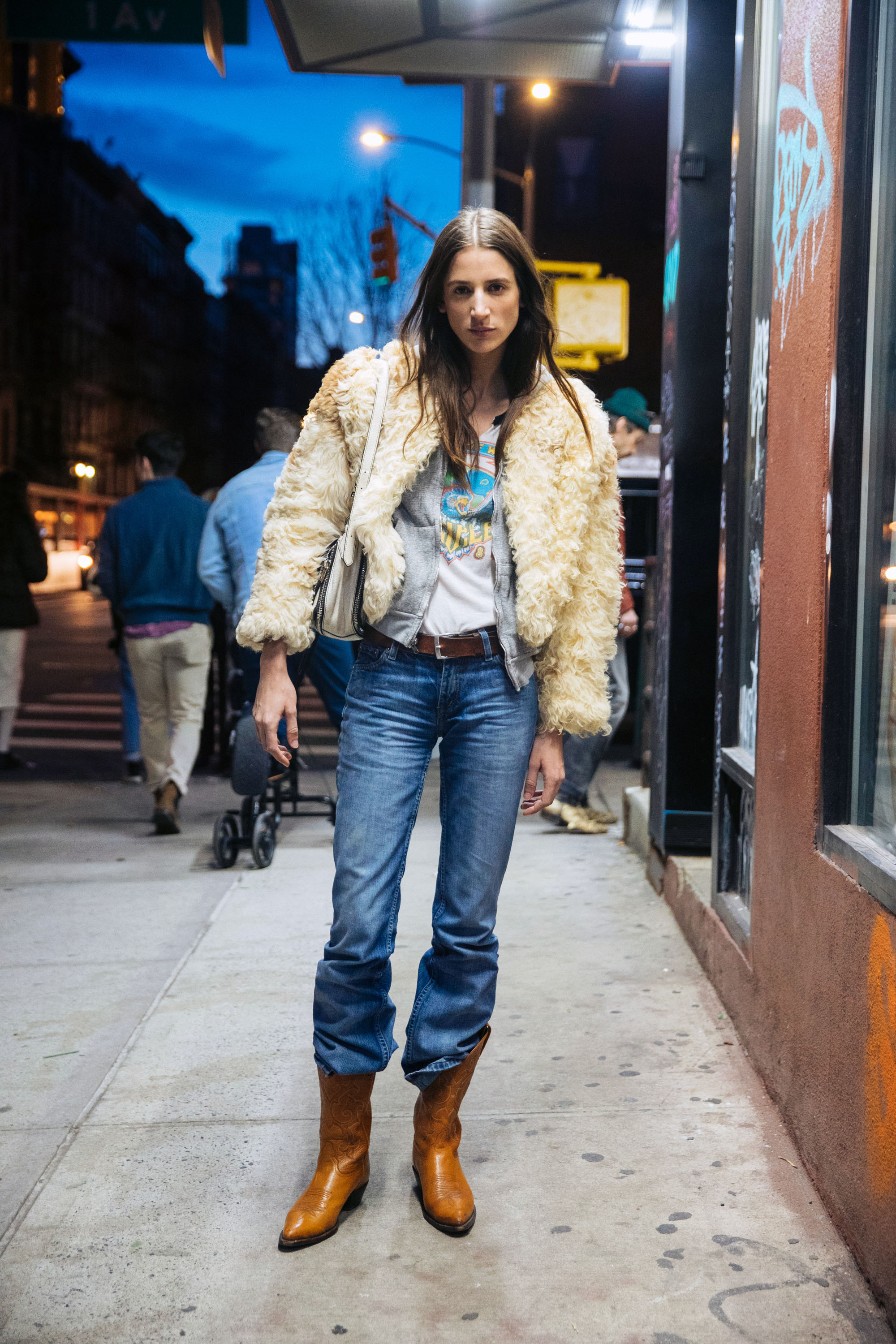 A woman wears a fur coat, graphic tee, jeans tucked into cowboy boots.