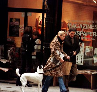 A photo of Carolyn Besette-Kennedy walking her dog in a leopard print coat.