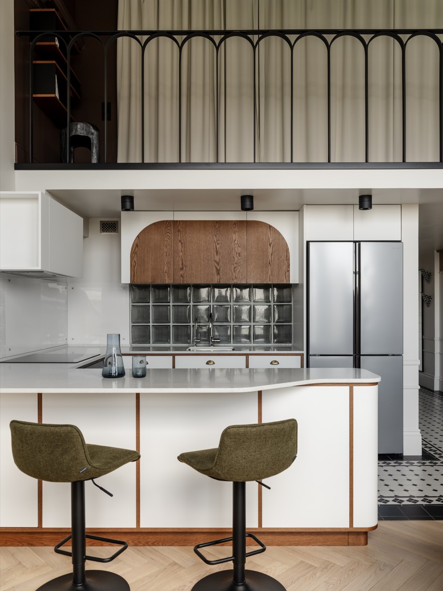 An industrial style kitchen with a curved breakfast bar, green swivel chairs, and wooden accents