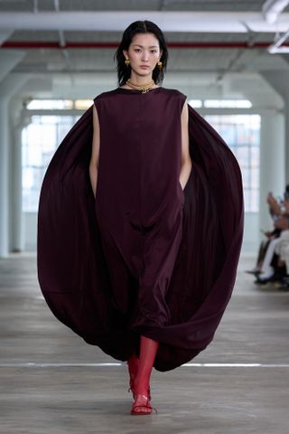 A woman wearing a purple cape dress and red tights on Tibi's Spring 2025 runway.