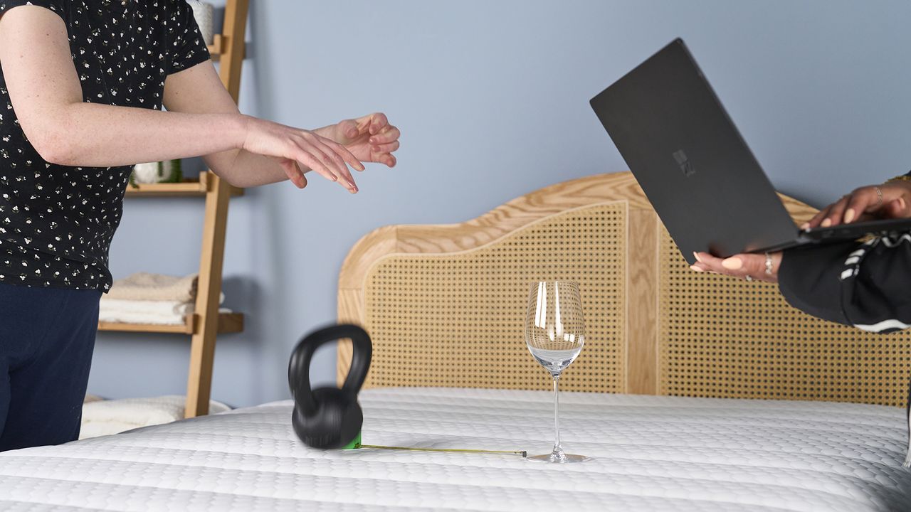 A wine glass balancing on Brooklyn Bedding CopperFlex mattress as a kettlebell is dropped next to it, testing motion isolation