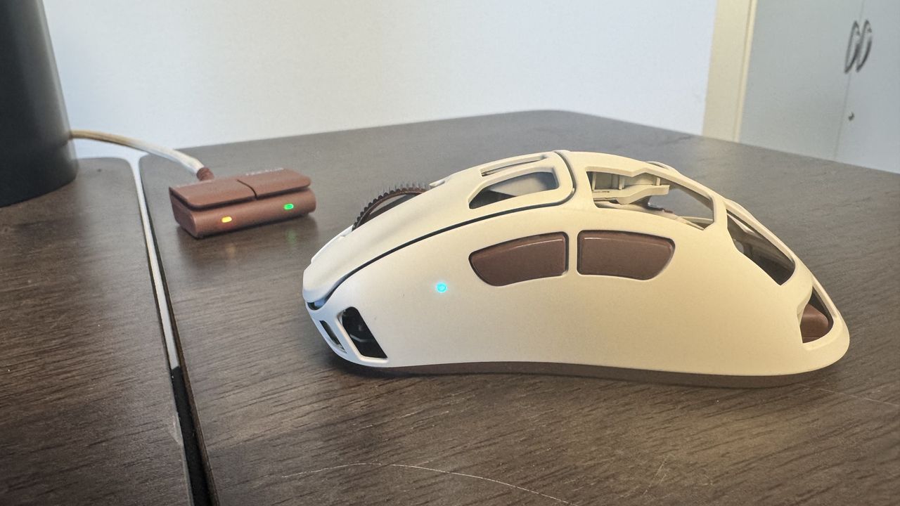 The Pulsar Feinmann F01 Noctua Edition gaming mouse from the left with its light on, near the connector on a wooden desk