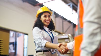 A woman in a construction hat shakes hands with her new employer.
