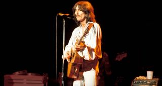 George Harrison wears all white and plays an acoustic guitar during his 1974 Dark Horse tour.