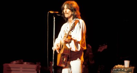 George Harrison wears all white and plays an acoustic guitar during his 1974 Dark Horse tour.
