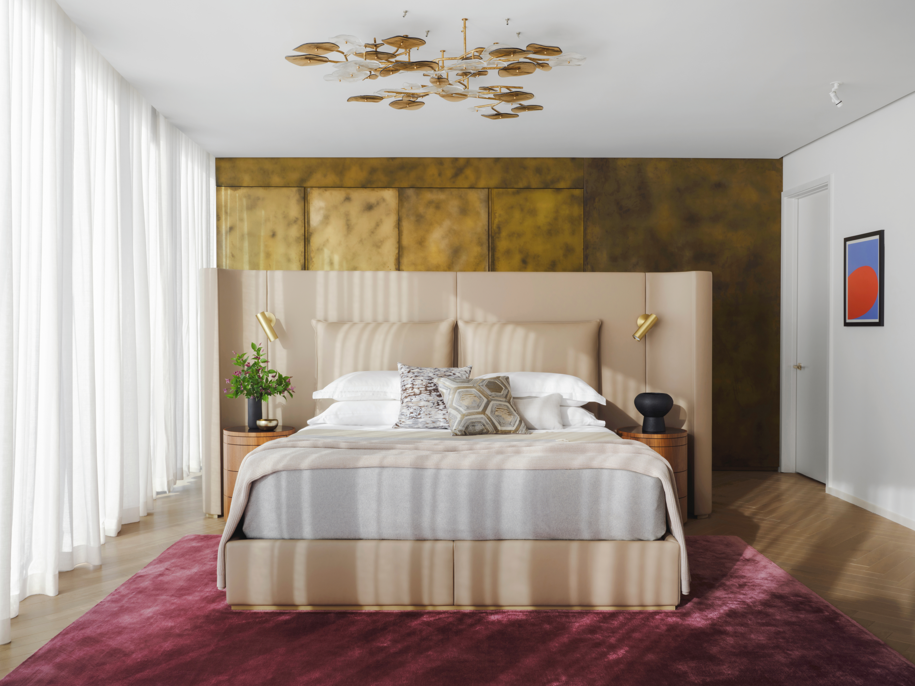 Bedroom with cream leather extended headboard, brass-effect wallcovering, deep pink rug and white sheer curtains