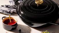 A polished jet black Le Creuset braiser on a table beside a mini cocotte