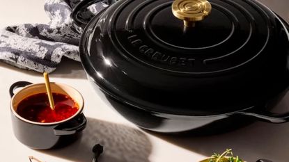 A polished jet black Le Creuset braiser on a table beside a mini cocotte