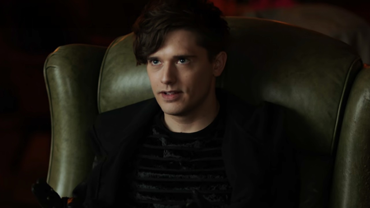 Andy Mientus as Heatley Rathaway wearing a black hoodie, sitting in a chair on The Flash.