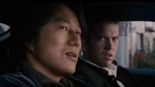 Han in foreground and Sean in background both sitting in a car in Tokyo Drift