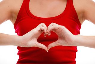 A woman places her hands in the shape of a heart over her chest.