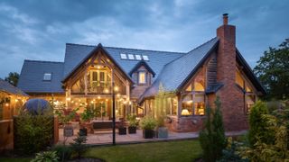 exterior of large brick and timber clad oak frame home at night