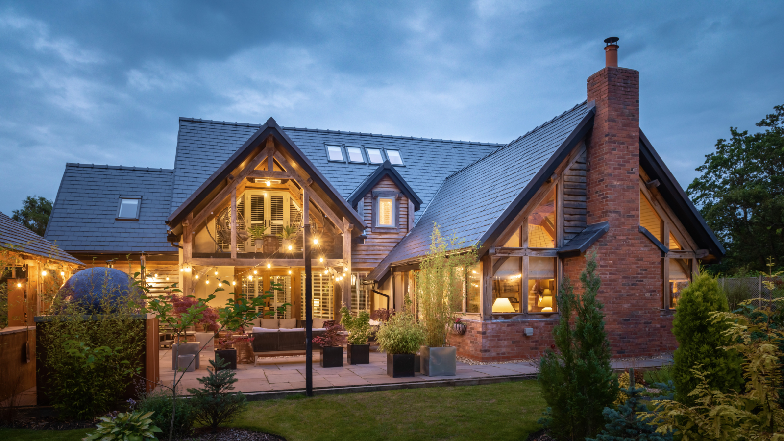 exterior of large brick and timber clad oak frame home at night