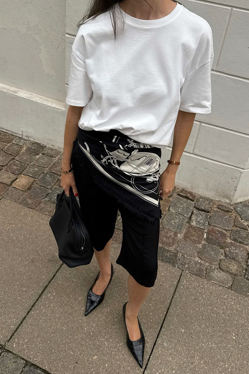A woman wearing a white t-shirt with black culottes and pointed-toe black shoes