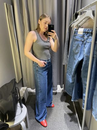 Woman in mirror wears grey vest, blue jeans and red shoes