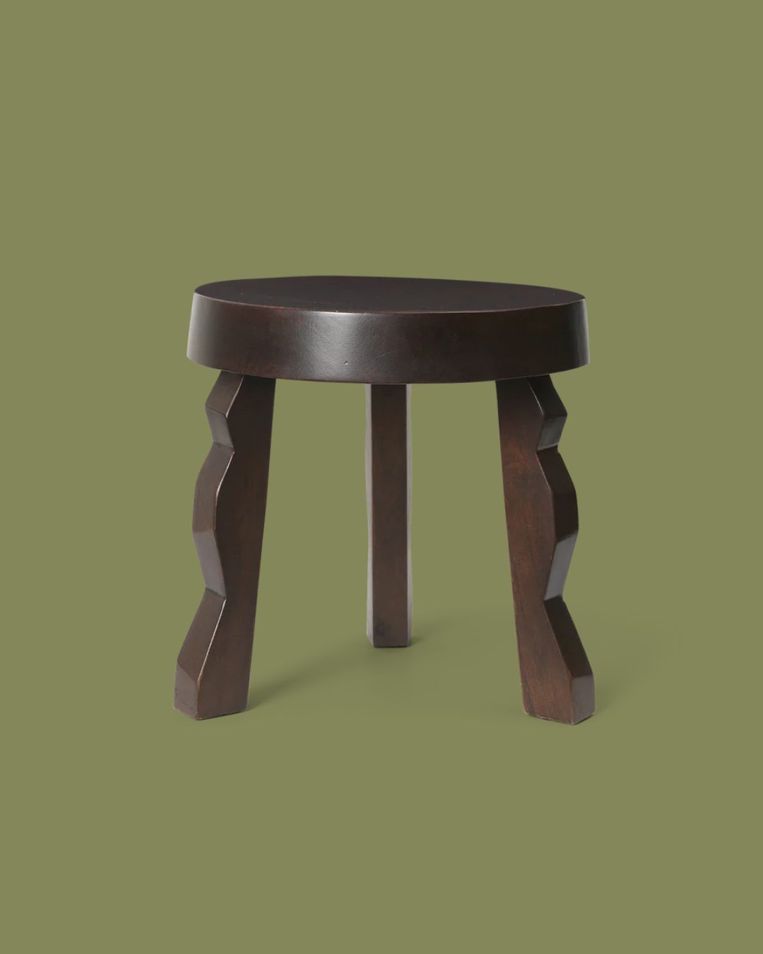 Ferm Living Faye Stool in Dark Stained Mango Wood against dark green background.