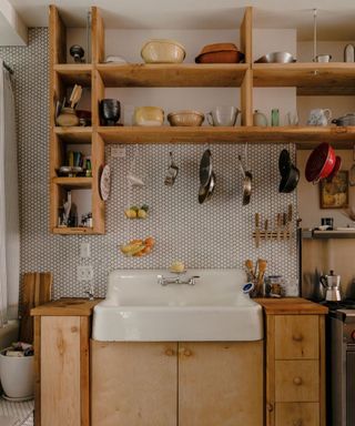 A wooden kitchen with a large white sink, tiled backsplash, and open wooden shelving