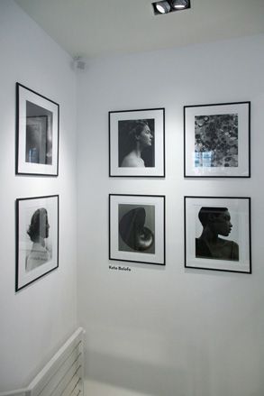 6 framed images in the corner of the exibithion room, hanging on a white wall