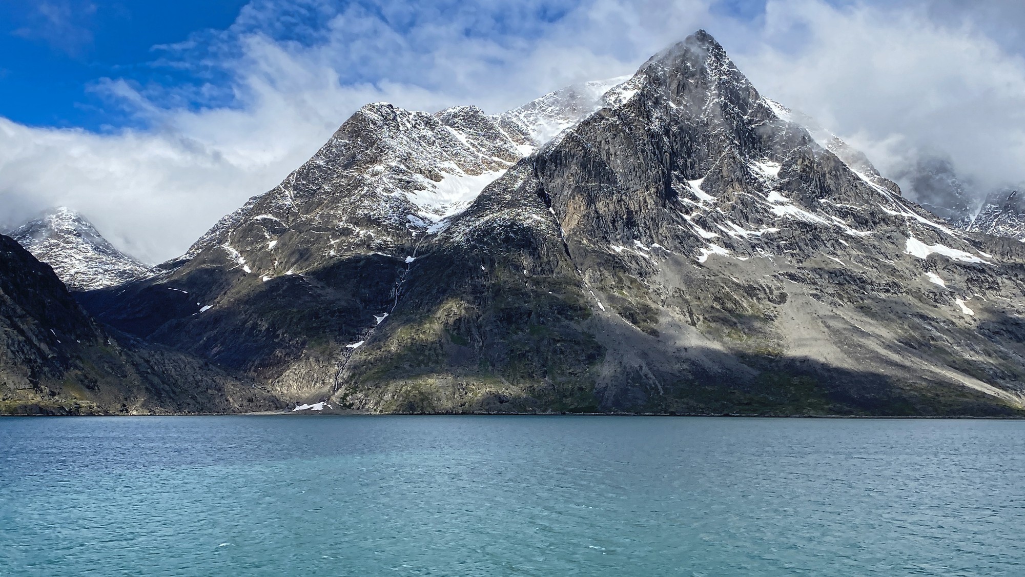 stunning fjord with water below and towering mountains with snow on top rise into the deep blue sky.