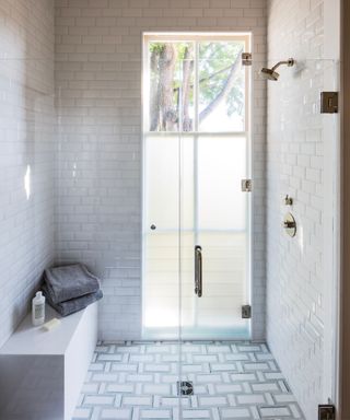 A small bathroom with a walk-in shower covered in white tiles and a woven floor tile layout