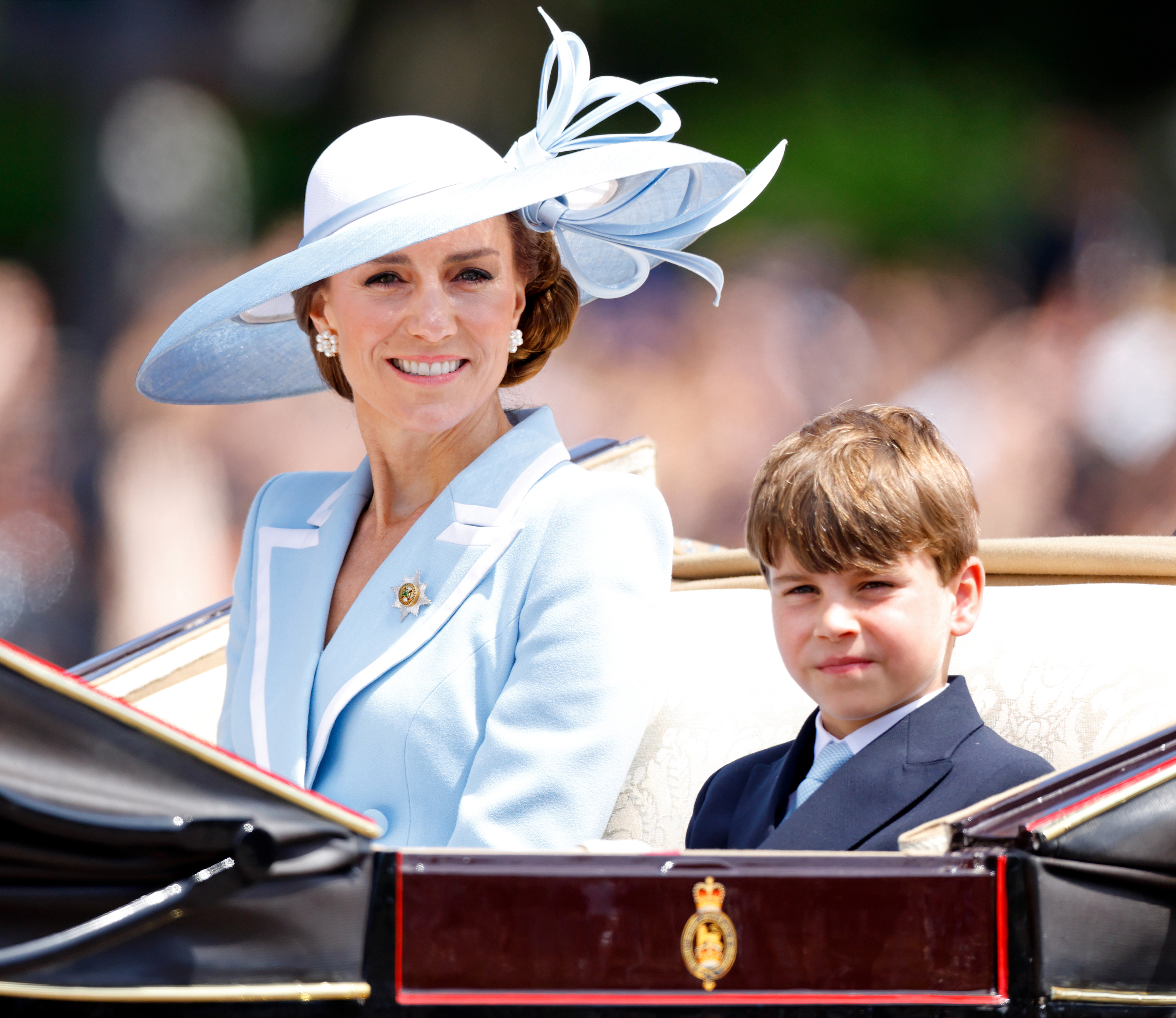 Prince Louis wears a navy blazer with gold buttons and a white shirt with a baby blue tie, which matched brother Prince George and mom Princess Kate's Trooping the Colour outfits