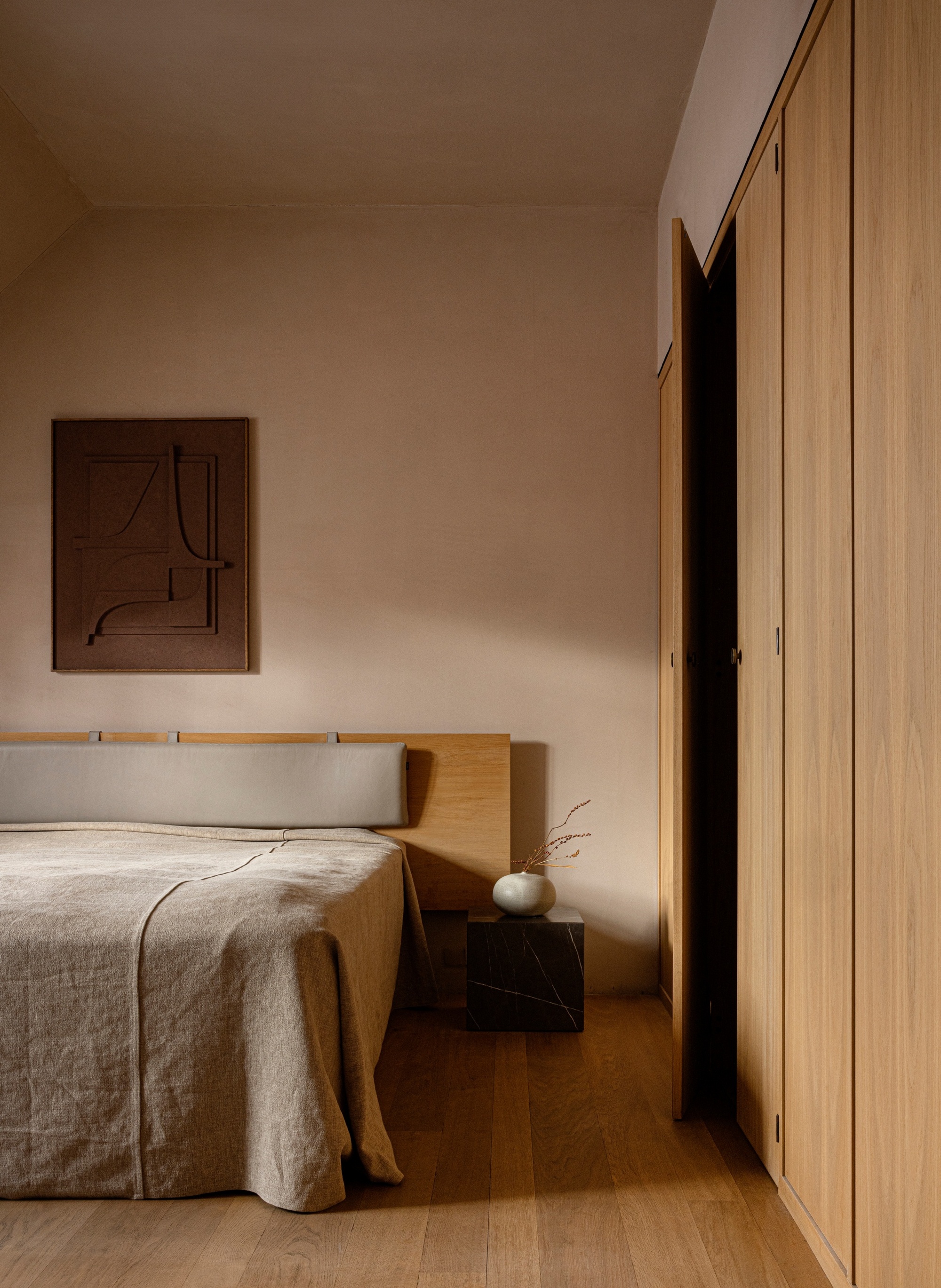 A Scandi minimalist bedroom with wooden flooring, built-in closet and headboard, and natural linens on the bed