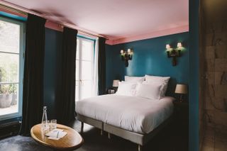 A dark blue hotel bedroom with a pink ceiling